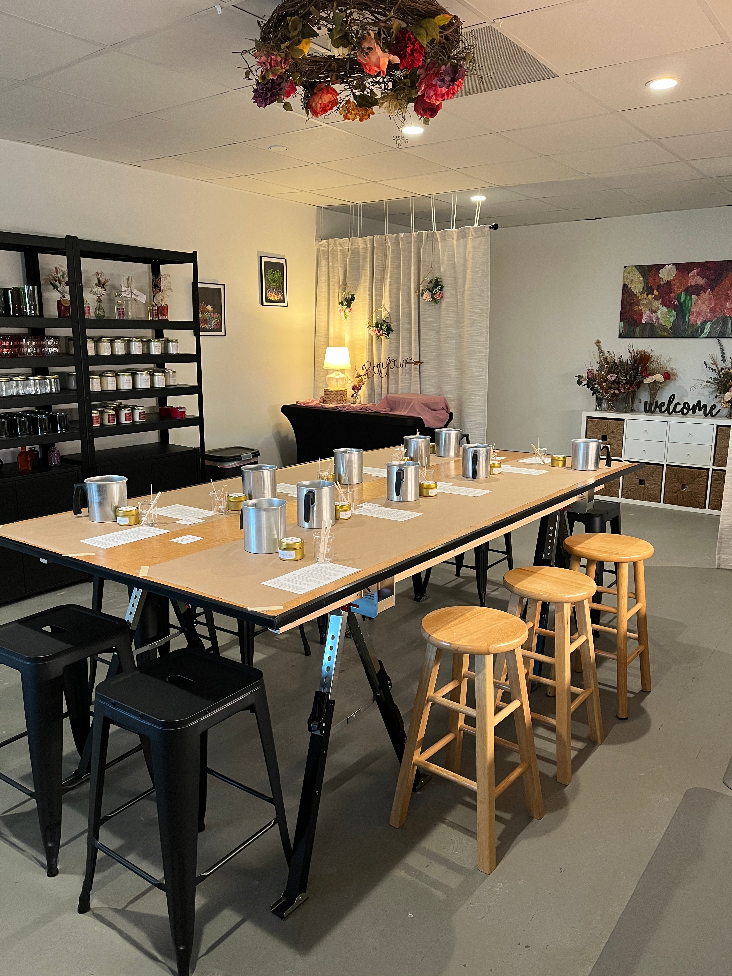 A long wooden table set up for candle-making class with metal pouring pots and other craft supplies in a candle studio.